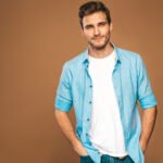 Portrait of handsome smiling stylish hipster lumbersexual businessman model dressed in jeans clothes. Fashion man. Posing on golden background